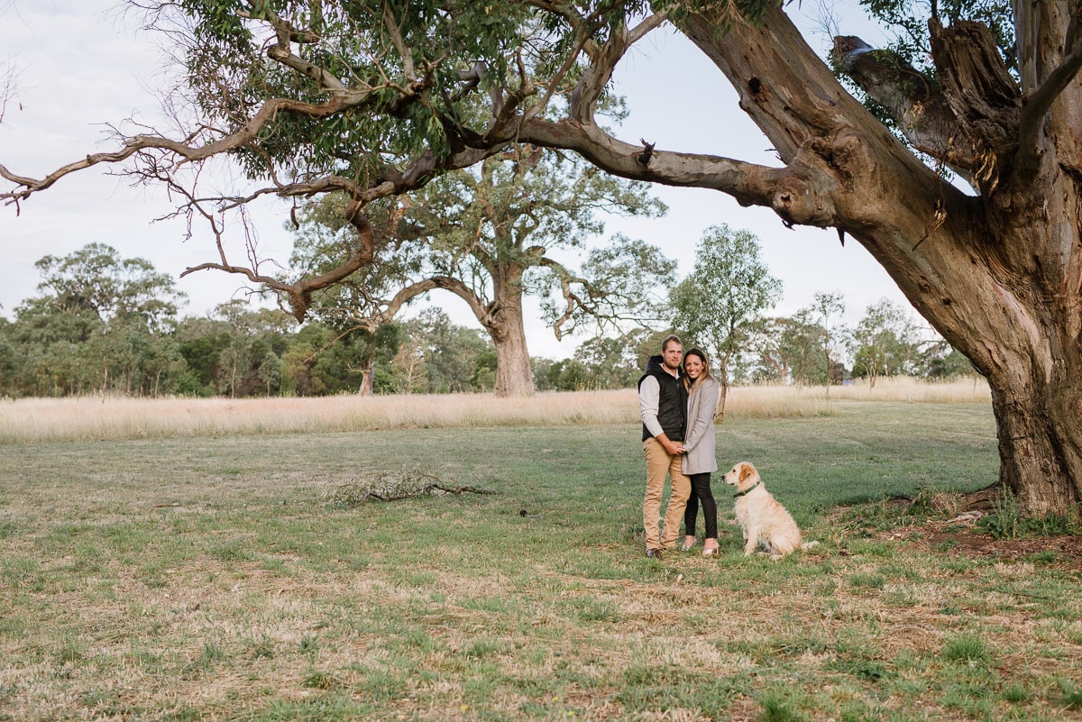 Couple with their dog stood under a tree