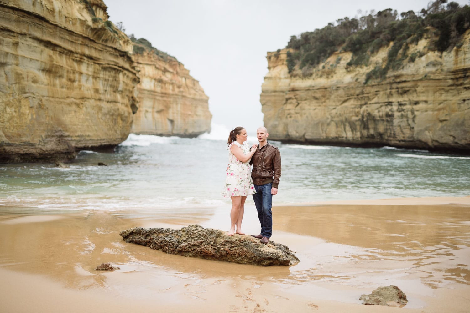 Couple stand on a rock near the ocean