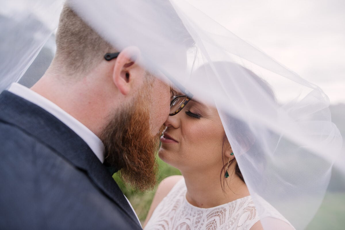 Bride and groom kiss under a veil after their wedding