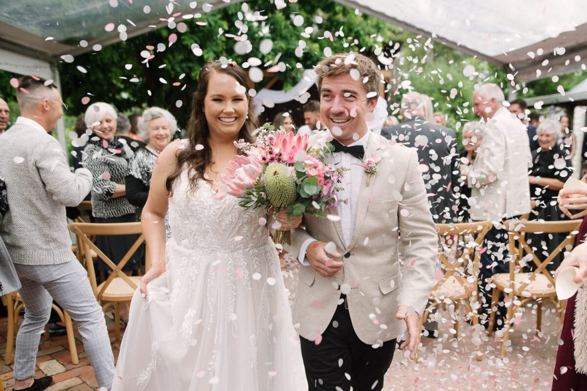 Bride and groom walk through flower petals at their Bootmaker's cottage wedding in Birregurra.